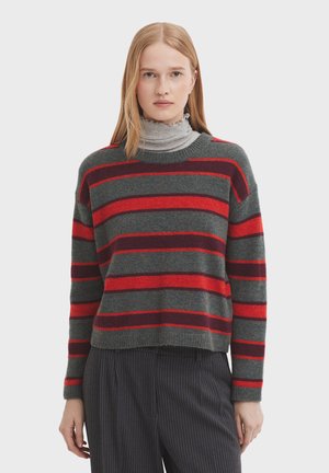 Der gestrickte Pullover hat eine graue Basis mit breiten roten und dunkelroten Streifen. Er hat einen gerippten Rundhalsausschnitt und Bündchen, kombiniert mit einem grauen Rollkragenpullover darunter.