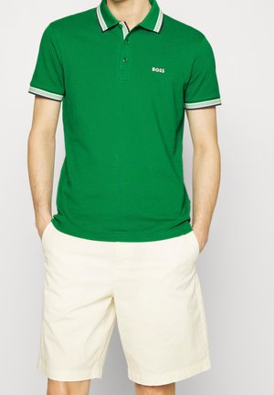 Grünes Baumwoll-Polohemd mit einem Kragen, das schwarze und weiße Akzente aufweist, kombiniert mit hellbeigen Shorts. „BOSS“-Logo auf der Brust.
