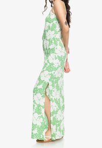 Zelené květinové maxi šaty s volným střihem, bez rukávů, bočními rozparky a vzory bílého hibiskusu a listů. Prodyšná textilie.