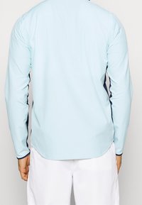 Ljust blå långärmad skjorta med marinblå sidodetaljer och kontrasterande mudd. Slät textur, atletisk passform, minimalistisk design.