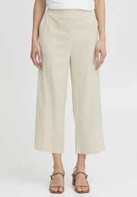 Lichtbeige wijde broek van textuurlinnen, met een elastische tailleband en een vloeiende silhouette, gecombineerd met bruine sandalen.