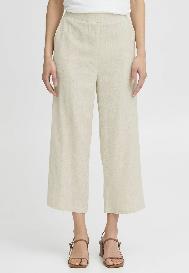 Pantalon large beige clair en lin texturé, doté d'une taille élastique et d'une silhouette fluide, assorti à des sandales marron.