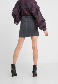 Černá džínsová sukně s třepeným lemem a dvěma zadními kapsami, spárovaná s vzorovanou blůzou a černými kotníkovými botami na podpatku.