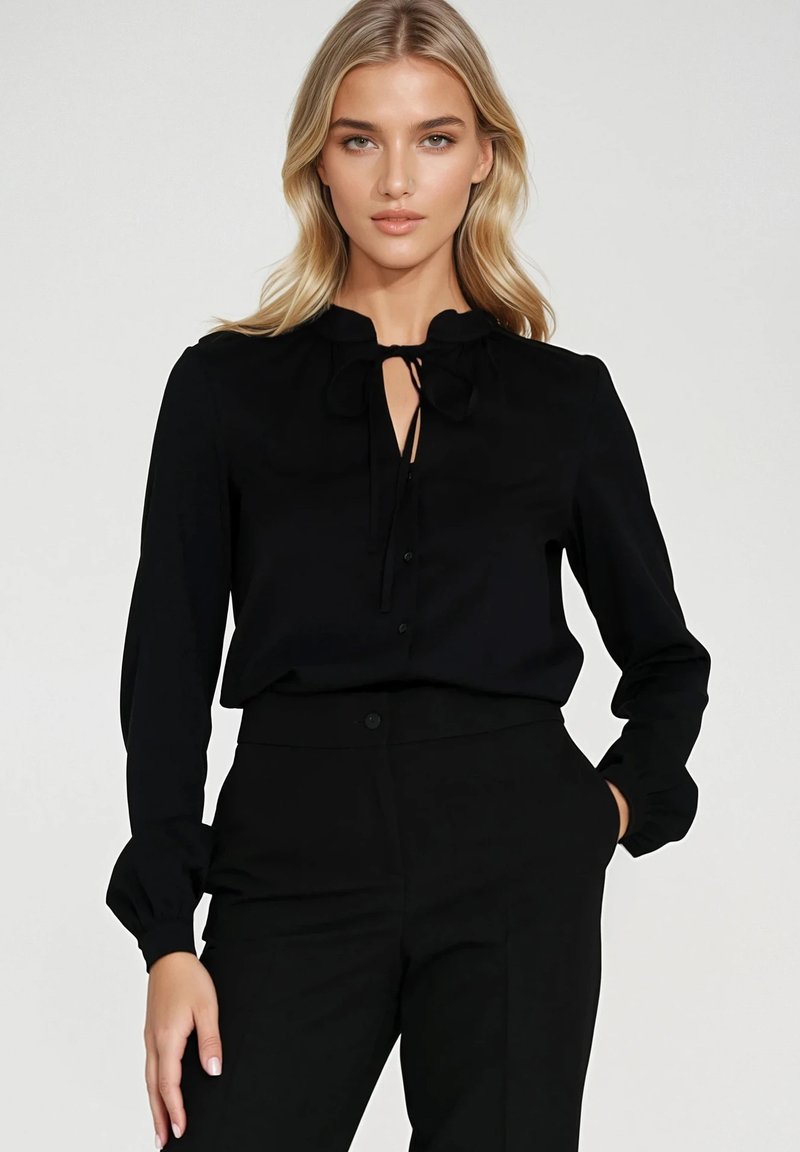 Czarna bluzka z kokardą przy szyi, długim rękawem i zapięciem na guziki. Gładki materiał, dopasowany krój i subtelny połysk.