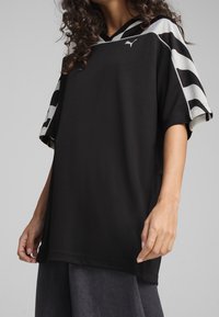 Maillot de sport noir surdimensionné à manches courtes, avec un tissu texturé et un motif ondulé contrastant noir et blanc sur les manches.