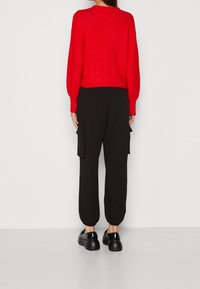 Rode gebreide trui, zwarte cargobroek met zijzakken en zwarte schoenen met een ronde zool. Eenvoudige, casual silhouet.