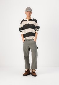 Polo en maille rayée noir et crème avec un col, associé à un pantalon gris clair et des bottines à cheville marron. Coupe décontractée, tissu texturé.