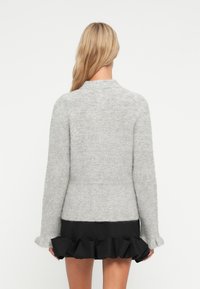 Ανοιχτό γκρι πλεκτό πουλόβερ με στρογγυλή λαιμόκοψη και μακριά μανίκια, με ραμμένα μανίκια και συνδυασμένο με μια μαύρη φούστα με ρίγες.