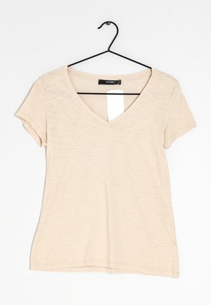 T-shirt beige à manches courtes avec encolure en V, suspendu à un cintre en métal noir avec une étiquette de prix blanche vierge, sur fond blanc.
