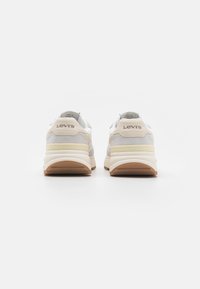 Baskets blanches et beige en matériaux de daim et en mesh ; semelle intermédiaire épaisse ; semelle extérieure en caoutchouc marron ; logo "Levi's" sur le talon.