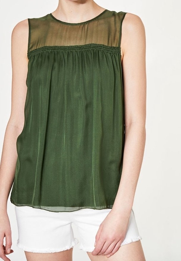 Blouse sans manches vert olive avec empiècement transparent et détail froncé, portée avec un short blanc à ourlet effiloché.