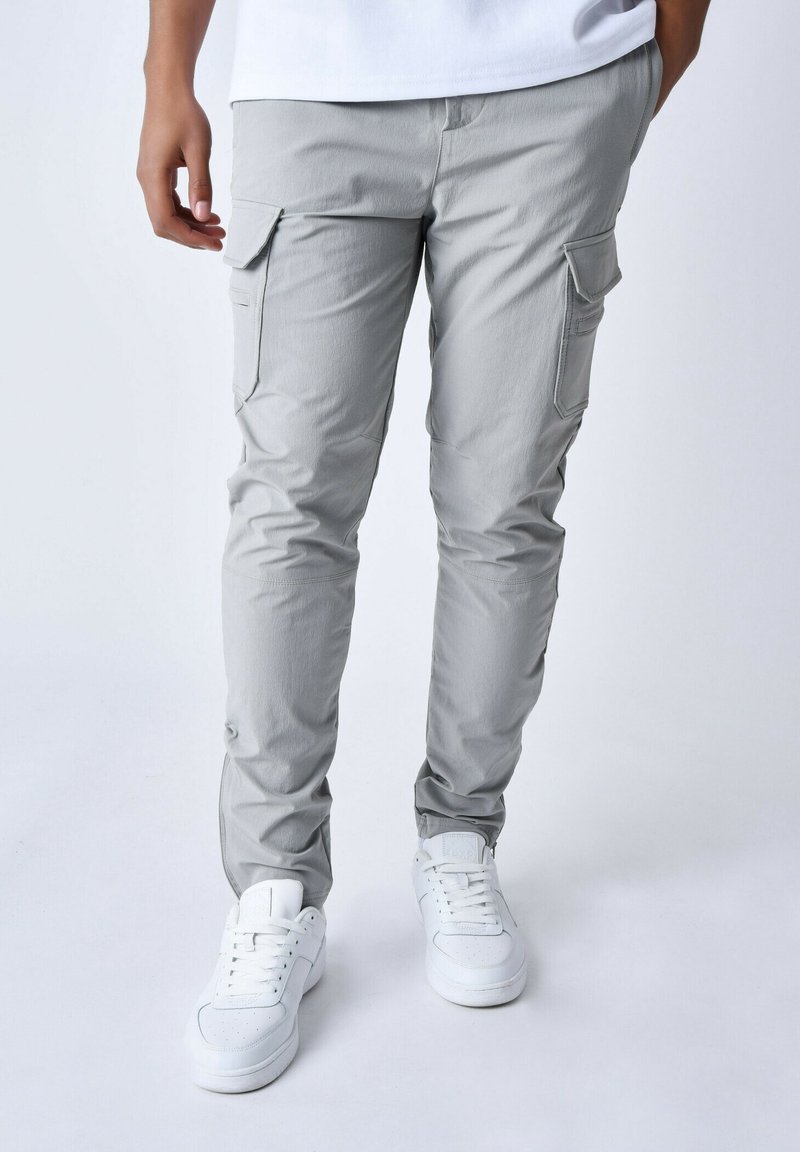 Pantalon cargo gris clair avec plusieurs poches, coupe fuselée, en tissu léger, associé à des baskets blanches.