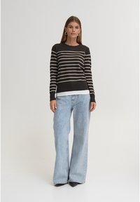 Oprijeta pulover s črtami v temno rjavi barvi z bež progami, kombiniran s svetlo modrimi kavbojkami širokih hlačnic. Pulover ima okrogel izrez in rebraste manšete.