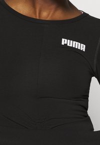 Nahaufnahme eines schwarzen Sportoberteils mit weißem Puma-Logo auf der Brust, getragen von einer Person.