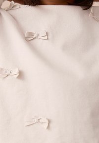 Light pink fabric top featuring multiple small, textured bows in a lighter shade, made of ribbon with a simple knot detail.
