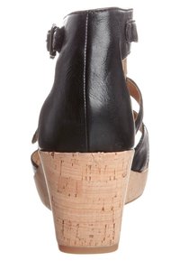 Sandalo con tacco in pelle nera, suola in sughero a zeppa, dotato di cinturino alla caviglia regolabile e design aperto con dettagli intagliati.