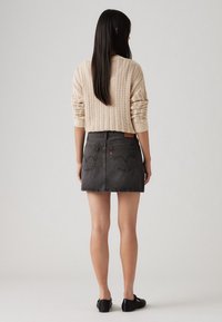 Pull en maille beige clair avec une texture côtelée et des épaules tombantes, associé à une mini jupe en denim noire avec des poches arrière.