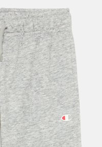 Ανοιχτό γκρι φόρμα με απαλή υφή, ελαστική μέση και μικρό λογότυπο σε κόκκινο και μπλε στο κάτω αριστερό πόδι.