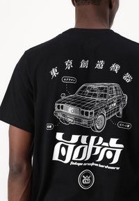 Svart T-skjorte med et hvitt bilgrafikk med etiketter på japansk, tekst som sier "tokyo creative hardware", og detaljerte designelementer.