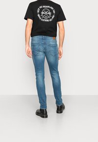 Camiseta negra con estampado gráfico en blanco en la parte trasera, combinada con vaqueros ajustados de color azul claro y botines negros. Costuras detalladas en los vaqueros.