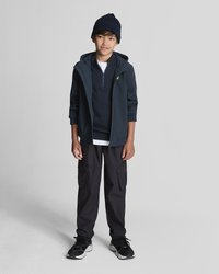 Giacca sportiva navy sopra un maglione scuro, abbinata a pantaloni cargo neri e sneakers nere. Gli accessori includono un berretto di maglia navy.