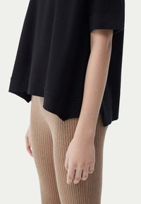 Svart, löst sittande t-shirt med korta ärmar och rundad nederkant, i kombination med ribbade, beigefärgade leggings. Slät tygstruktur.