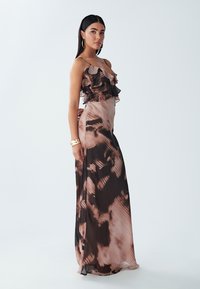 Maxi jurk in doorzichtig bruin en roze stof, met geschulpte schouderbanden, een aansluitende bodice en een vloeiende silhouet met abstracte patronen.