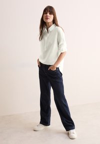 Lichtgroen overhemd met kraag en opgerolde mouwen, gecombineerd met donkerblauwe wijde jeans en witte sneakers. Eenvoudig, schoon ontwerp met minimale details.