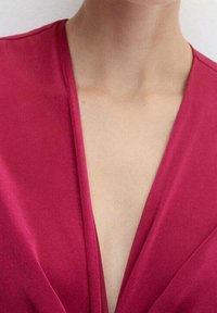 Blusa fucsia con un design a profonda scollatura a V e tessuto morbido e fluido. Costruzione senza cuciture con cuciture visibili minime.