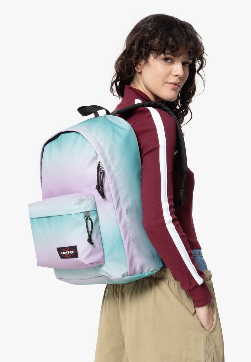 Zaino con design ombreggiato che sfuma dal blu chiaro al viola, realizzato in tessuto morbido, con una tasca frontale e zip nere.