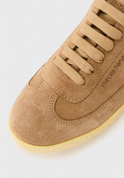Tan mockasin med tjocka beige snörningar och ljusgul sula, med "EMPORIO ARMANI" logotyp på sidan.
