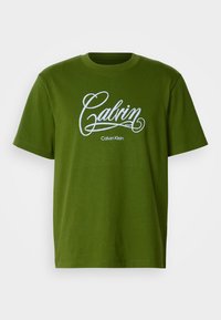 Green short-sleeve T-shirt with white "Calvin" script and "Calvin Klein" text centered on the front against a plain background.