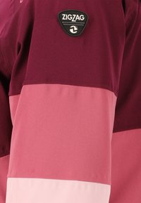Langarmjacket in bordeauxrood en roze tinten, met een zachte textuur, horizontale kleurvlakken en een zwart ZigZag logo patch.