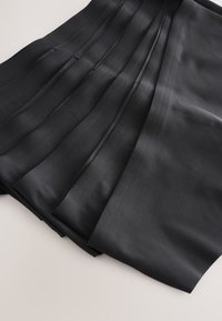 Tessuto nero pieghettato accuratamente piegato su una superficie chiara, che mostra una texture liscia e pieghe strutturate.