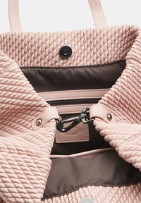 Teksturna ružičasta tkanina torba s magnetskim zatvaranjem, koja ima tamni interijer, zippered džep i kože trim detalje.