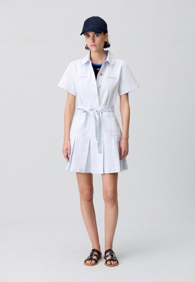 Robe utilitaire bleu clair avec un devant à boutons, des manches courtes et une taille ceinturée ; elle présente une jupe plissée et deux poches avant.