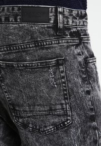 Czarne dżinsy denimowe o przetarciach, z logo na łatce i widocznymi szwami na tylnej kieszeni.