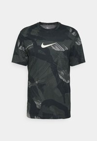 Svart och grön camouflagemönstrad Nike t-shirt tillverkad av mjukt tyg, med rund halsringning och en vit Nike-logotyp på bröstet.