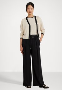 Krémový kardigán s čiernym lemom, kombinovaný s svetlým topom a čiernymi širokými nohavicami. Obsahuje gombíky a akcent opasku. Hladká textúra.