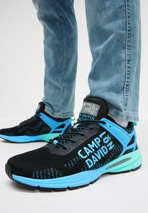 Sportliche Schuhe mit einem schwarzen Mesh-Obermaterial und blauen Akzenten, strukturiertem Design und einer grünlichen Sohle. Das Branding an der Seite lautet "CAMP DAVID."