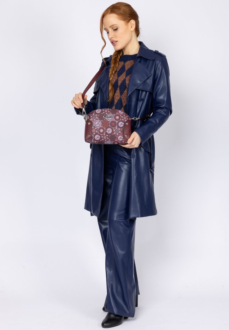 Ciemnoniebieski skórzany trencz na fakturowanym brązowo-granatowym swetrze, w połączeniu z małą bordo torebką z okrągłym wzorem i srebrnymi akcentami.