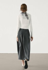 Chemise blanche à manches longues avec un col rond à l'arrière, associée à un pantalon large gris ample, et une écharpe à carreaux noir et blanc autour du cou.