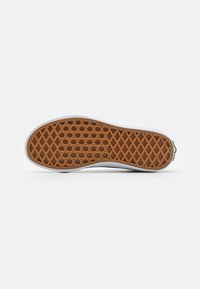 Suela de zapato con un patrón de panal en goma marrón, bordeada por un lateral blanco, con bordes suaves y un tacón redondeado.