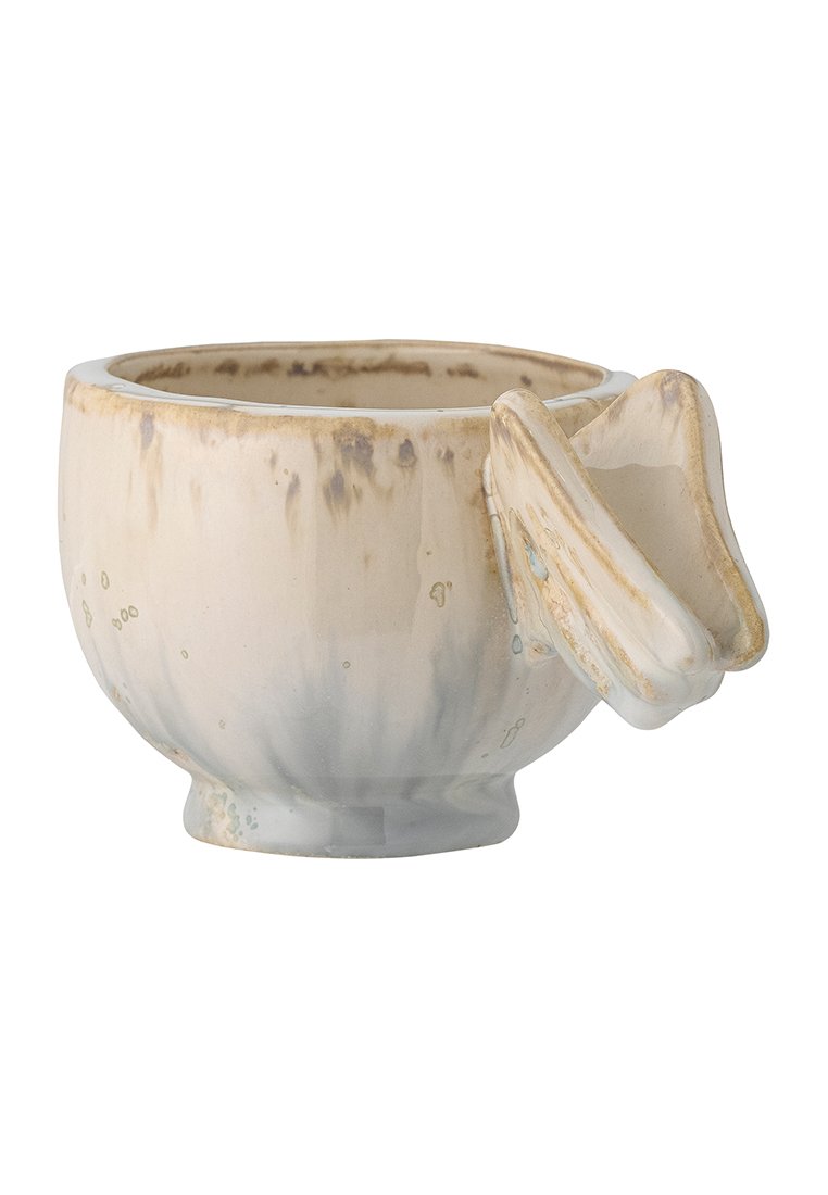 Ceramiczny kubek z błyszczącym białym i beżowym wykończeniem. Okrągłe ciało, rozszerzana podstawa oraz unikalny uchwyt przypominający mały dziób ptaka.