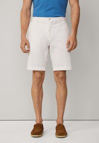 Shorts en coton blanc avec fermeture à bouton, devant plat, poches latérales et ourlets roulés, associés à des chaussures à enfiler en daim marron.