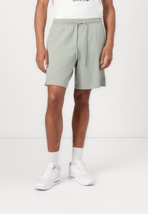 Lysgrønne bomuldsstøvler med elastisk livbånd og snoretræk, sidelommer og små logodetaljer. Båret med hvide sneakers og sokker.