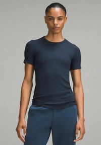 Navyblaues, kurzärmeliges, tailliertes T-Shirt aus glattem, elastischem Stoff. Runder Ausschnitt und subtile Nähte. Kombiniert mit passenden blauen Sporthosen.