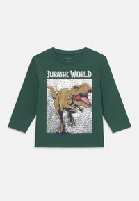 Zöld, hosszú ujjú póló, amelyen egy üvöltő dinoszaurusz grafikája és a "Jurassic World" felirat található, textúrázott nyomtatott háttéren.