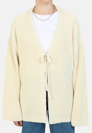 Crème-kleurige gebreide cardigan met een diepe V-hals, striksluiting en brede mouwen. Heeft een gestructureerd oppervlak en een geribbelde zoom.