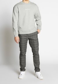 Šedá mikina s bílým nápisem "Just do it.", kombinovaná se štíhlými šedými kostkovanými kalhotami a bílými teniskami, s hladkou texturou.